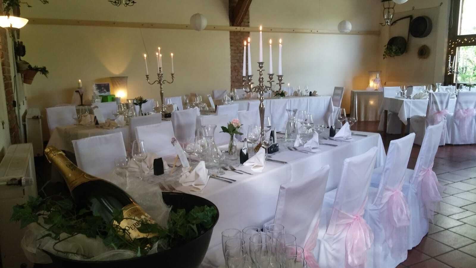 Un salón de banquetes con largas mesas dispuestas para un evento formal, que incluye manteles blancos, cristalería y candelabros.