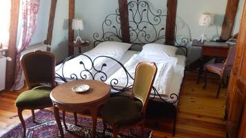 A bedroom with a bed, two chairs, a small table, a nightstand, and a desk with a lamp.