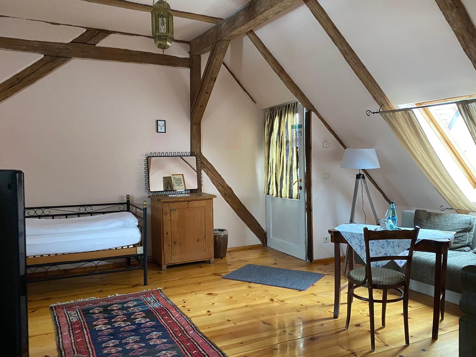 Een knus zolderkamer met een bed, een houten kast, een bureau met stoel en een raam met gordijnen.