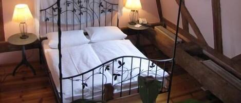 A four-poster bed with a canopy, two bedside lamps, and a hanging lantern in a room with wooden beams and a window with sheer curtains.