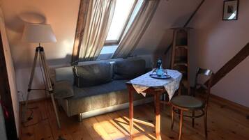 Une pièce mansardée chaleureuse, avec un canapé, une table et une lampe, ainsi qu’une chaise.