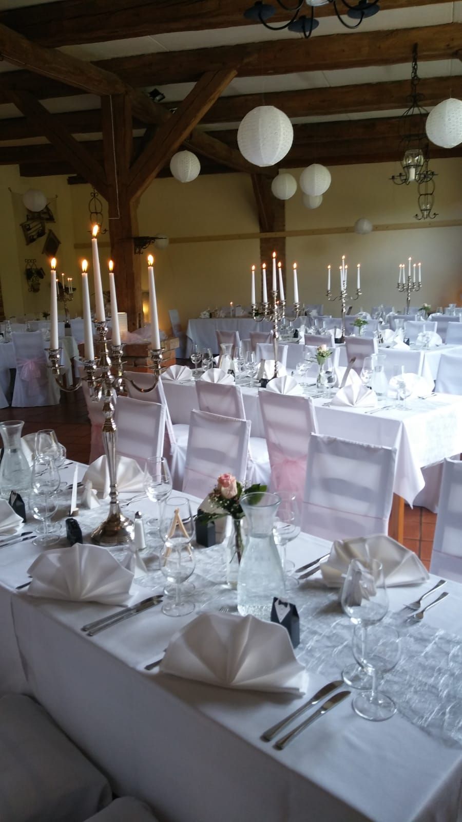 A banquet hall with tables set for a formal event, featuring white tablecloths, silverware, and candlelit candelabras.