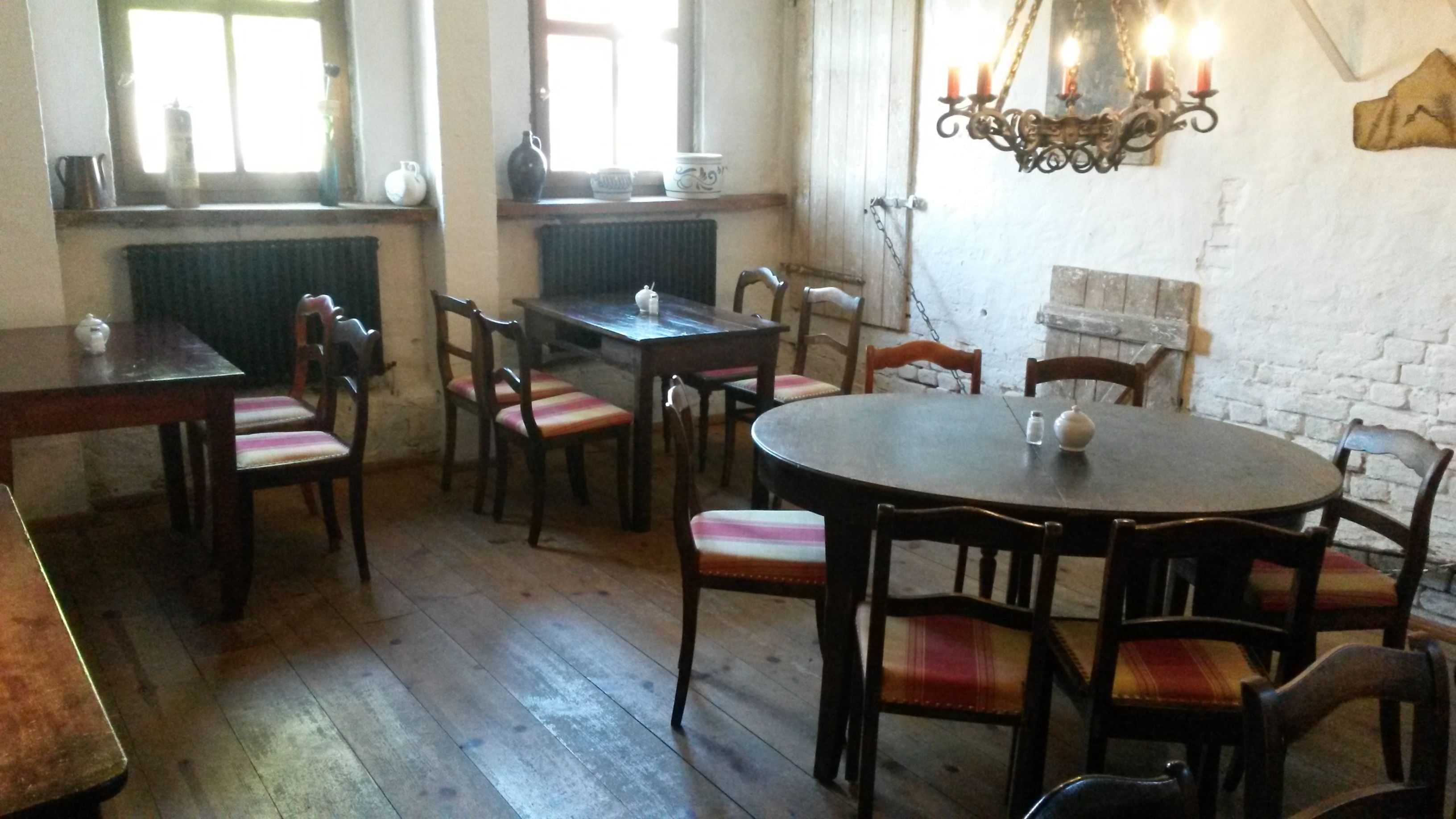 A dining area with wooden tables and chairs, a chandelier, and a white brick wall.