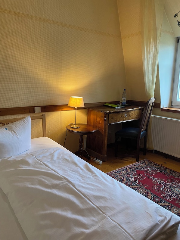Ett sovrum med en säng, ett skrivbord, en stol, en lampa och ett fönster med gardiner.