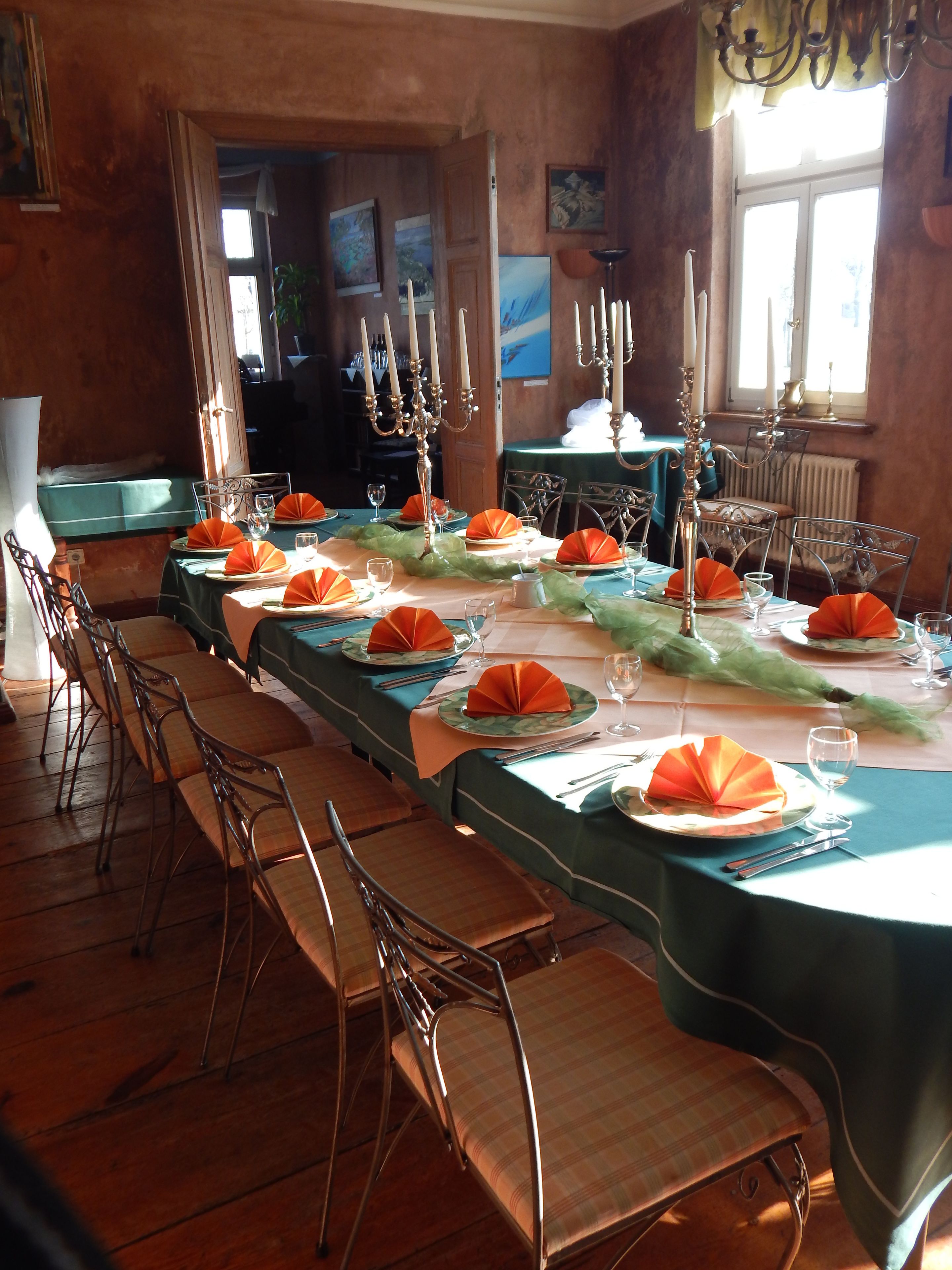 Una larga mesa de comedor dispuesta con sillas, candelabros y servilletas anaranjadas.