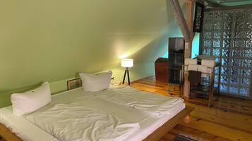 A bedroom with a large bed, a bedside table with a lamp, a wooden bench, and a view through a glass door.