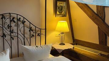 A bed with white linens, a metal headboard with a floral design, a bedside table with a lamp, and a wooden beam structure.