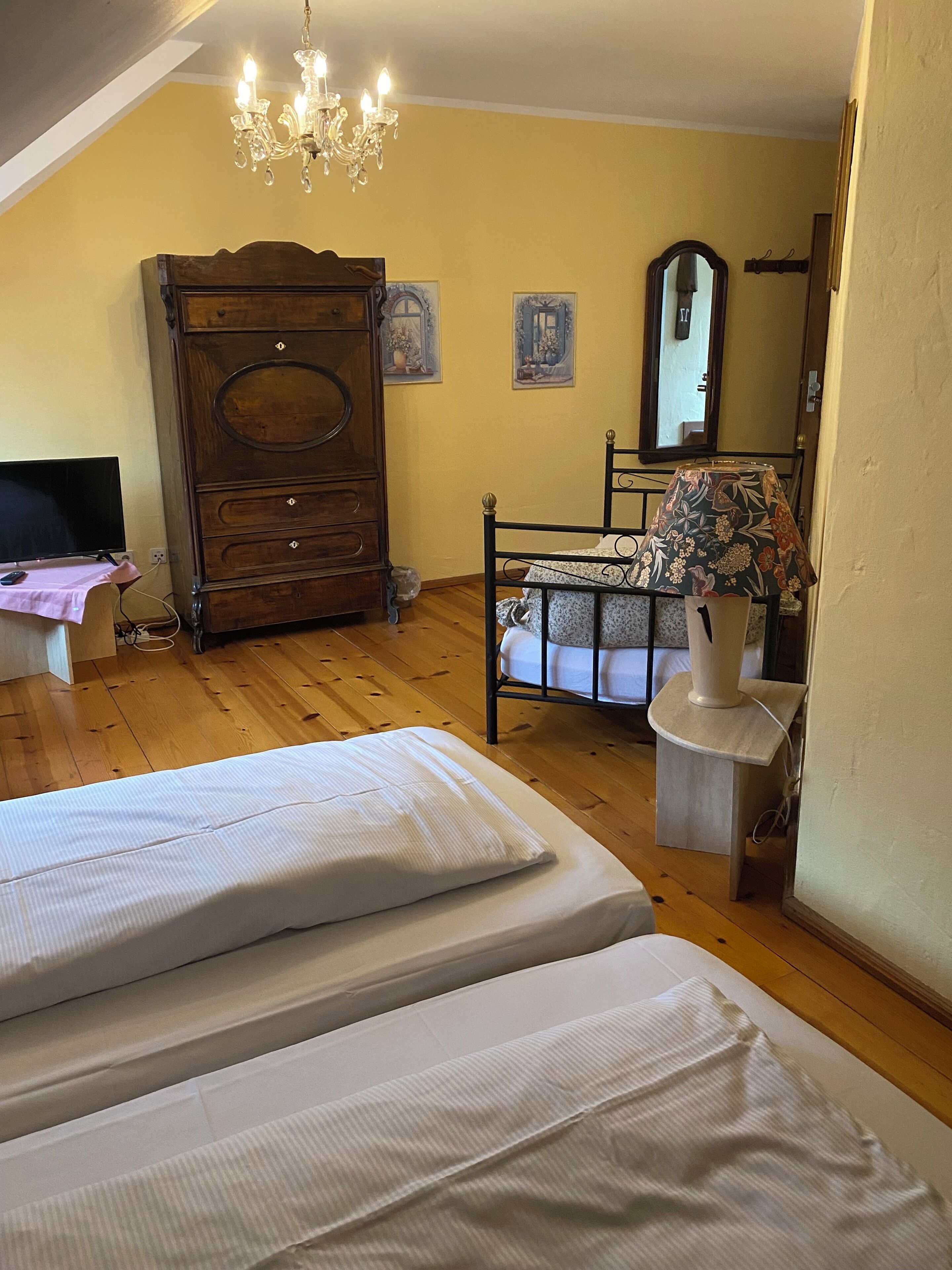 A bedroom with two beds, a wooden dresser, a chandelier, a mirror, and a table with a lamp.