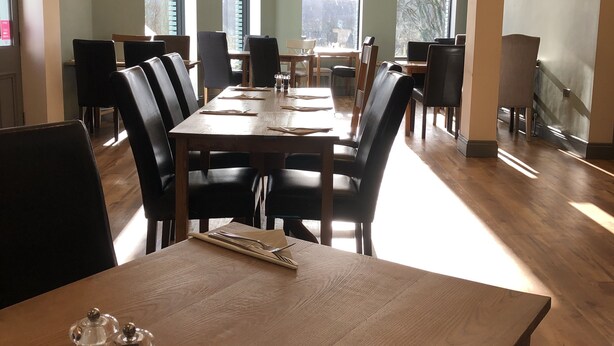 A dining area with a wooden table set for two, surrounded by chairs.