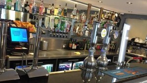 A bar area with a digital payment terminal, a cash register, and a variety of liquor bottles.