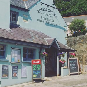 Un edificio con un letrero que dice "ROSE & CROWN RESTAURANT B&B COFFEE HOUSE" y un anuncio de Coca-Cola. Hay carteles que anuncian "GOURMET FRIDAYS" y "CURRY NIGHT" en la pared.