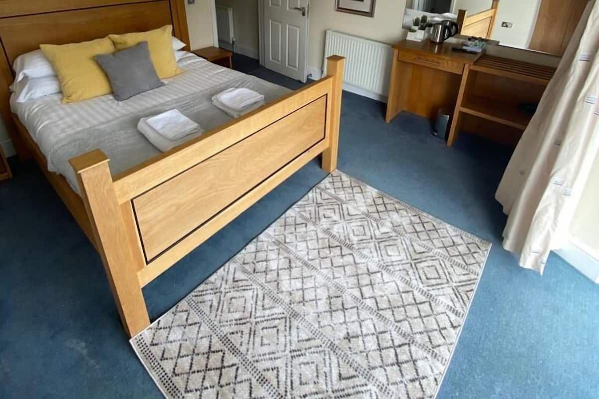 A bedroom with a wooden bed, a desk, a chair, a radiator, and a door.