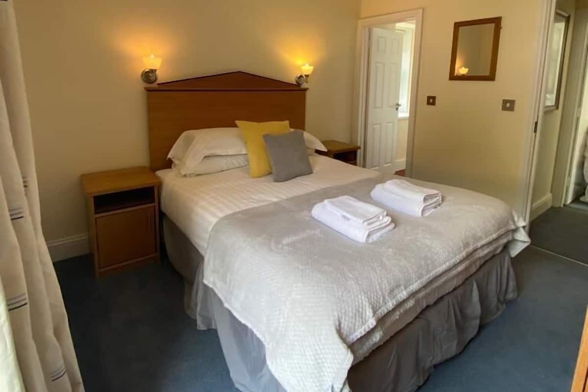 A neatly made bed with a grey bedspread and pillows, a wooden headboard, bedside lamps, and a small nightstand.