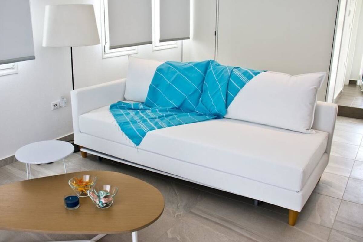 Ein modernes Hotelzimmer mit einem weißen Sofa, einem runden Holztisch und einem kleinen Beistelltisch.