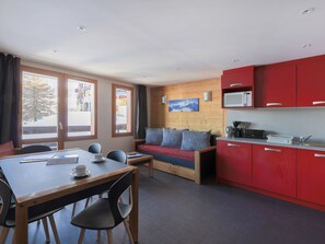 A modern room with a dining table, chairs, a sofa, and a kitchen area with red cabinets.
