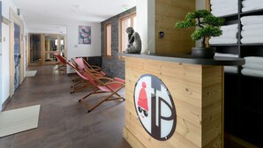 A reception area with a wooden counter, a reception desk, a potted plant, and a wall-mounted shelf with towels.