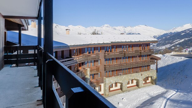 A multi-story building with a wooden facade and stone arches, set against a snowy mountain backdrop.