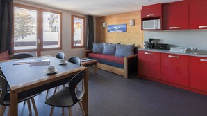 A modern room with a dining table, chairs, a sofa, and a kitchen area with red cabinets.