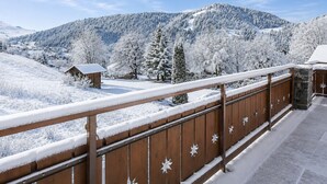 Ein Holzbalkon mit schneebedeckter Brüstung, der auf eine verschneite Berglandschaft blickt.