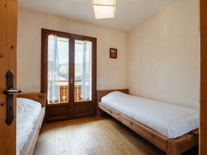 A small, simple room with two single beds, a wooden door, and a view of a balcony.