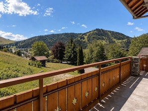 A wooden balcony with a view of a mountainous landscape and a small building in the distance.