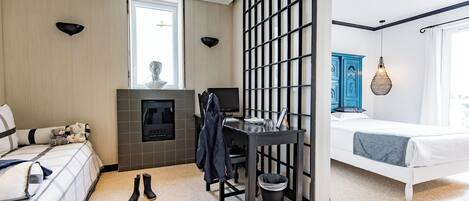 Una habitación de hotel moderna con cama, escritorio, silla, chimenea y un ventanal grande.