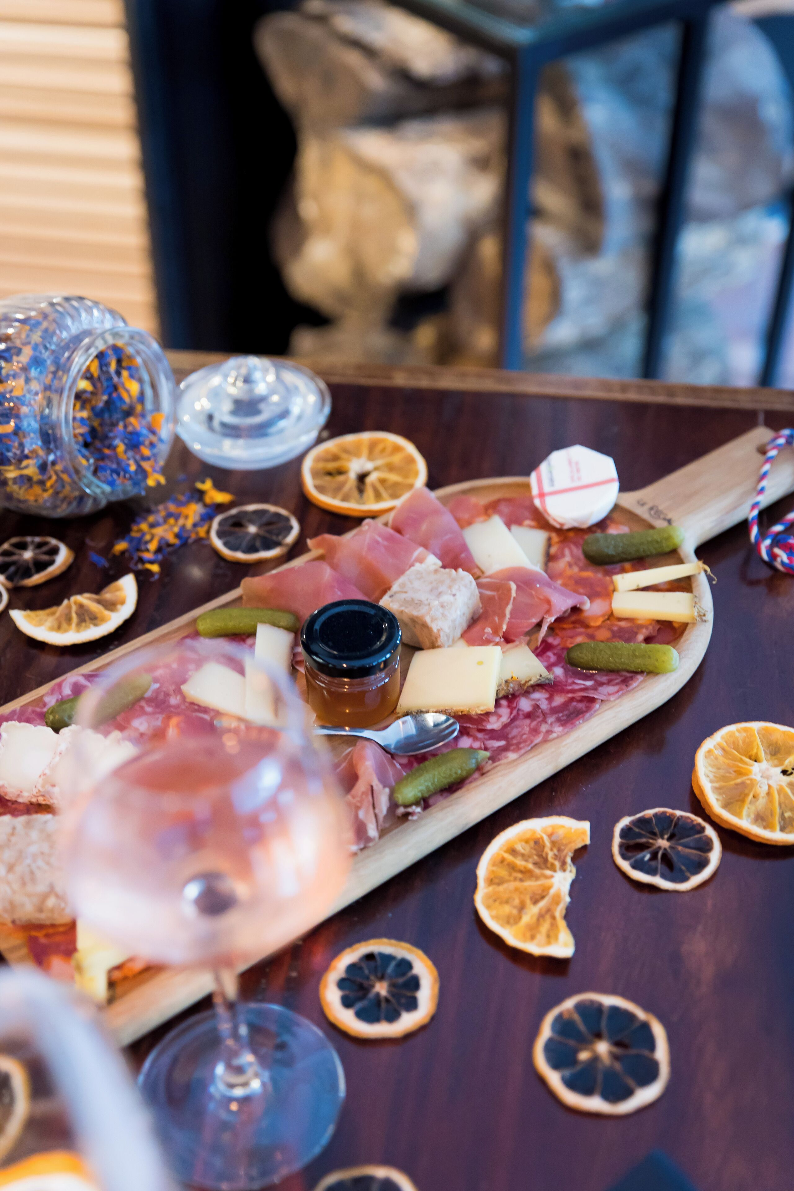 Eine Platte mit verschiedenen Wurstwaren, Käsesorten und eingelegten Gurken, dazu ein Glas Wein und getrocknete Orangenscheiben.