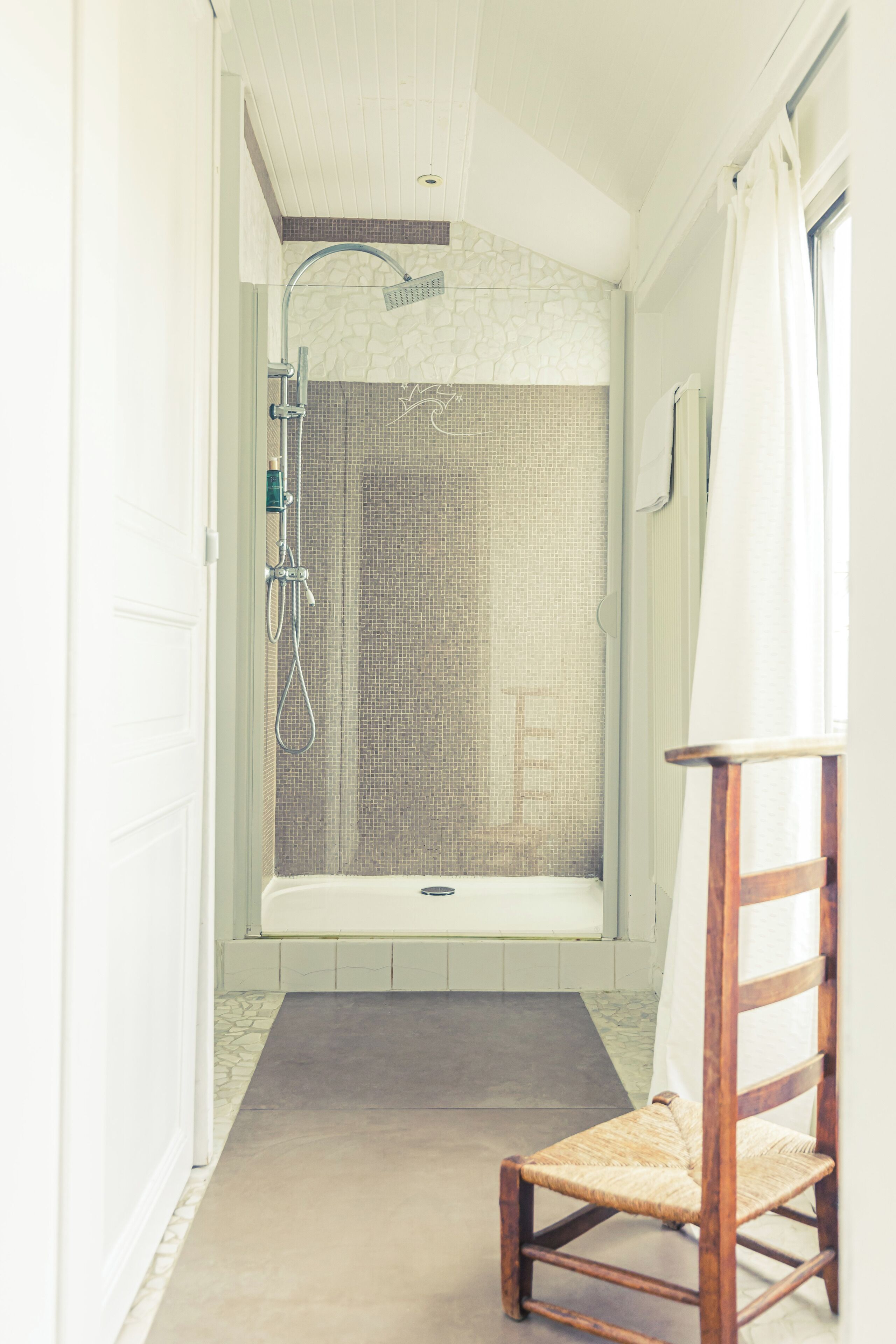 Una zona de ducha con puerta de cristal, una silla de madera y un revestimiento de azulejos.