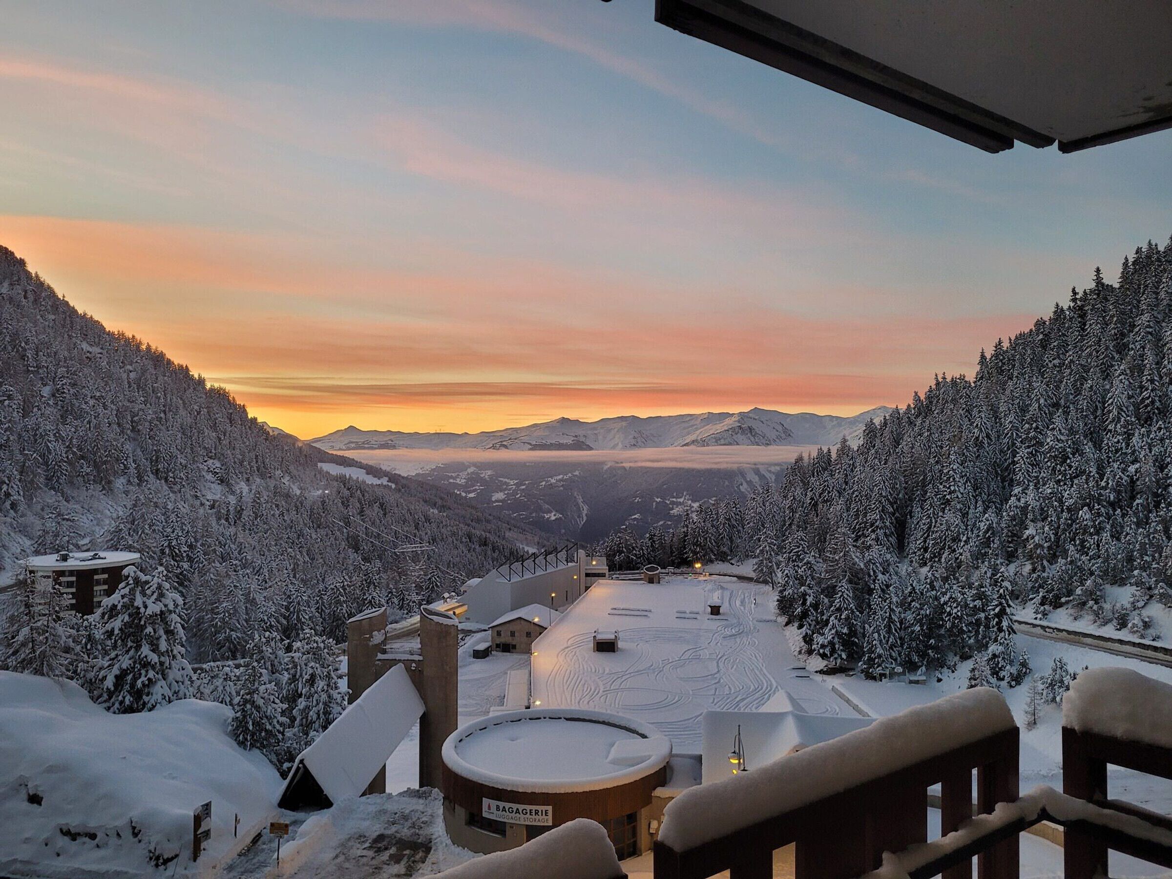 A snow-covered mountain landscape with a view of distant mountains and a sunset.