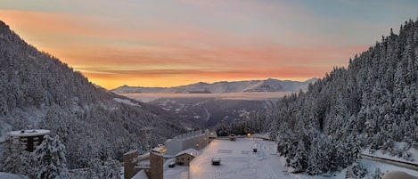 A snow-covered mountain landscape with a view of distant mountains and a sunset.