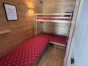 Una piccola stanza in legno con letti a castello, una citazione motivazionale incorniciata al muro e un piccolo ripiano.