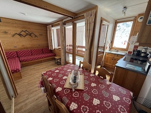 A cozy cabin with a wooden interior, a dining table with a heart-patterned tablecloth, a sofa with a red and white pattern, and a kitchen area with a sink and stove.
