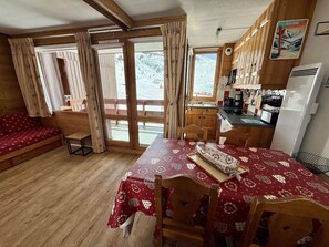 Una cabaña acogedora con mesa de comedor, sillas, sofá, armarios de madera, zona de cocina y ventanas grandes con cortinas.