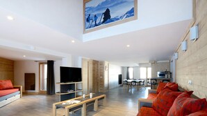 A spacious living area with a sofa, a coffee table, a TV, and a dining table with chairs.