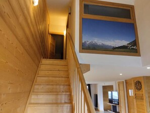 Un escalier en bois mène à une pièce dotée d’une grande fenêtre offrant une vue sur un paysage montagneux.