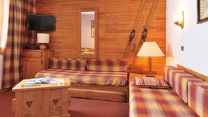 A cozy room with wooden paneling, a television, a mirror, skis leaning against the wall, and a sofa with plaid bedding. - 2-room apt for 5 in station center with balcony and pool (Plagne Bellecôte)