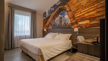 A hotel room with a bed, a desk, and a large mural of a bridge.