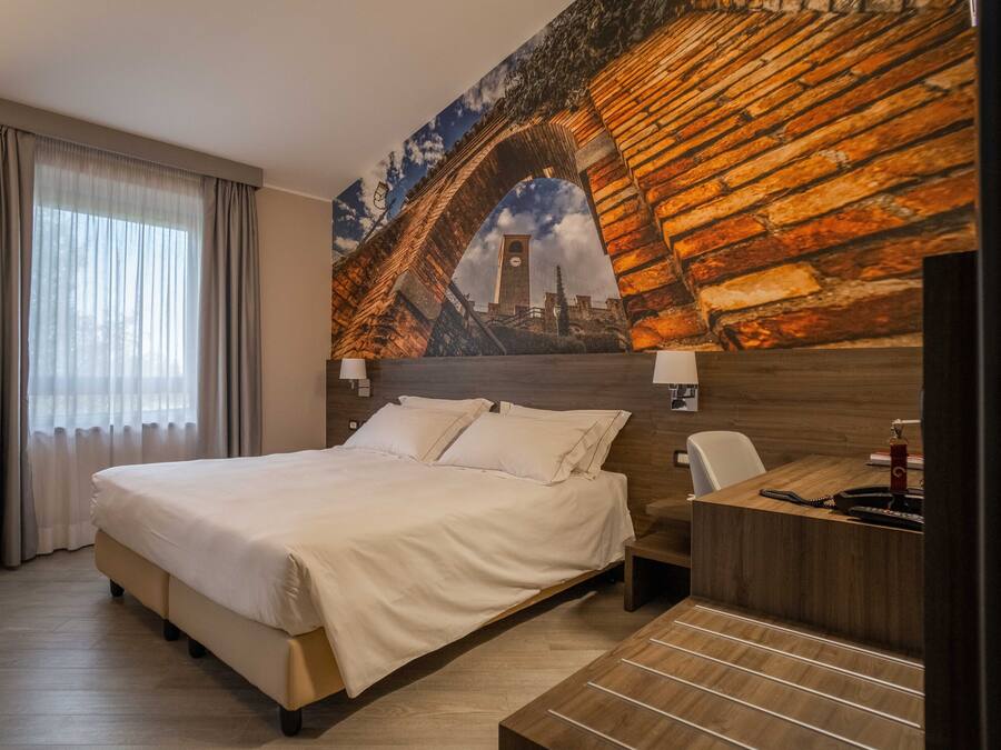 A hotel room with a bed, a desk, and a large mural of a bridge.