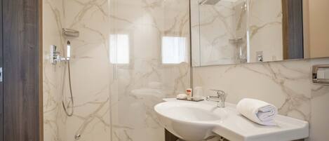 Un baño moderno con ducha de mármol, lavamanos y un espejo grande.