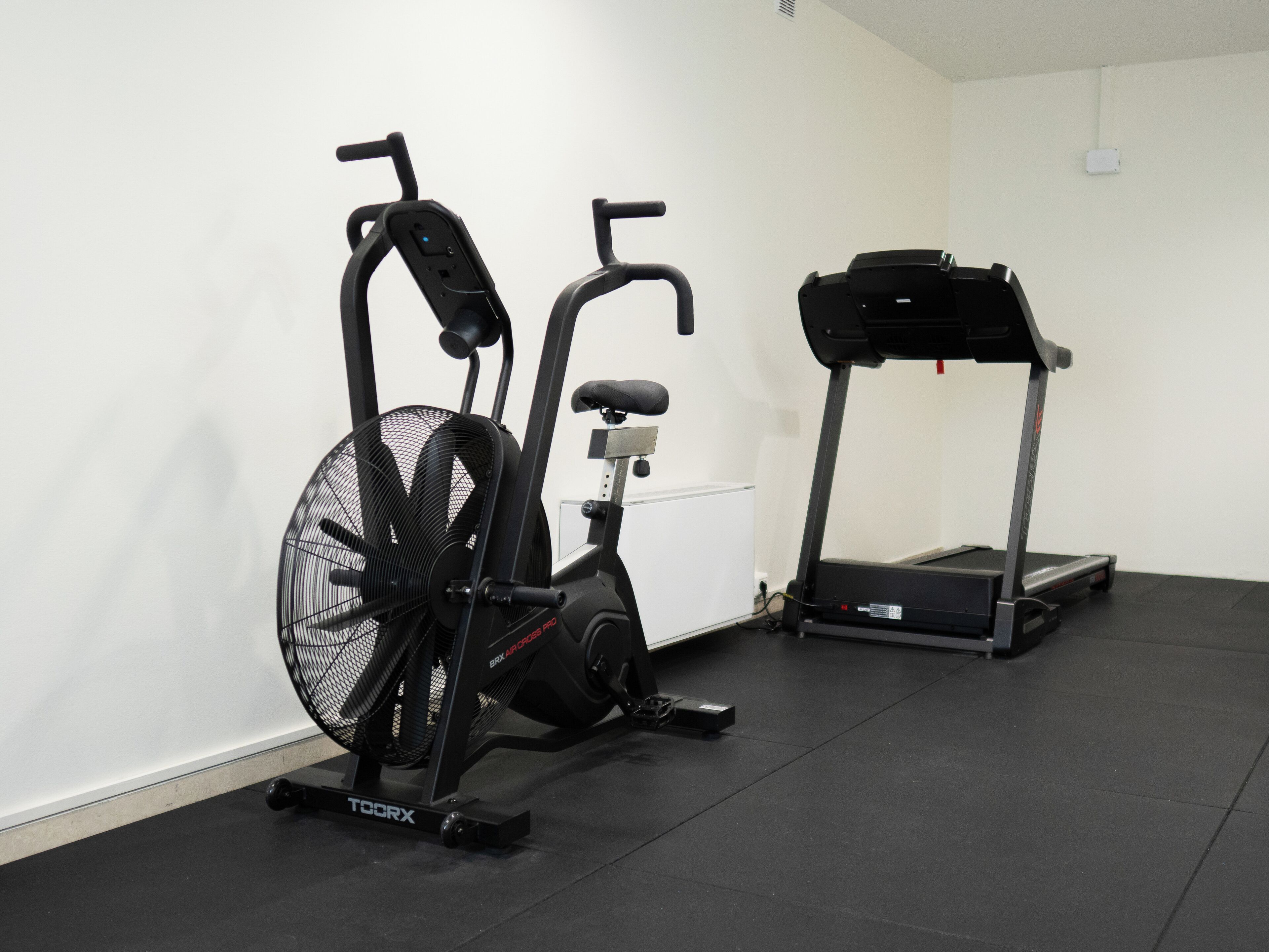 Une salle de sport équipée d’un vélo d’appartement, d’un tapis de course et d’un ventilateur.