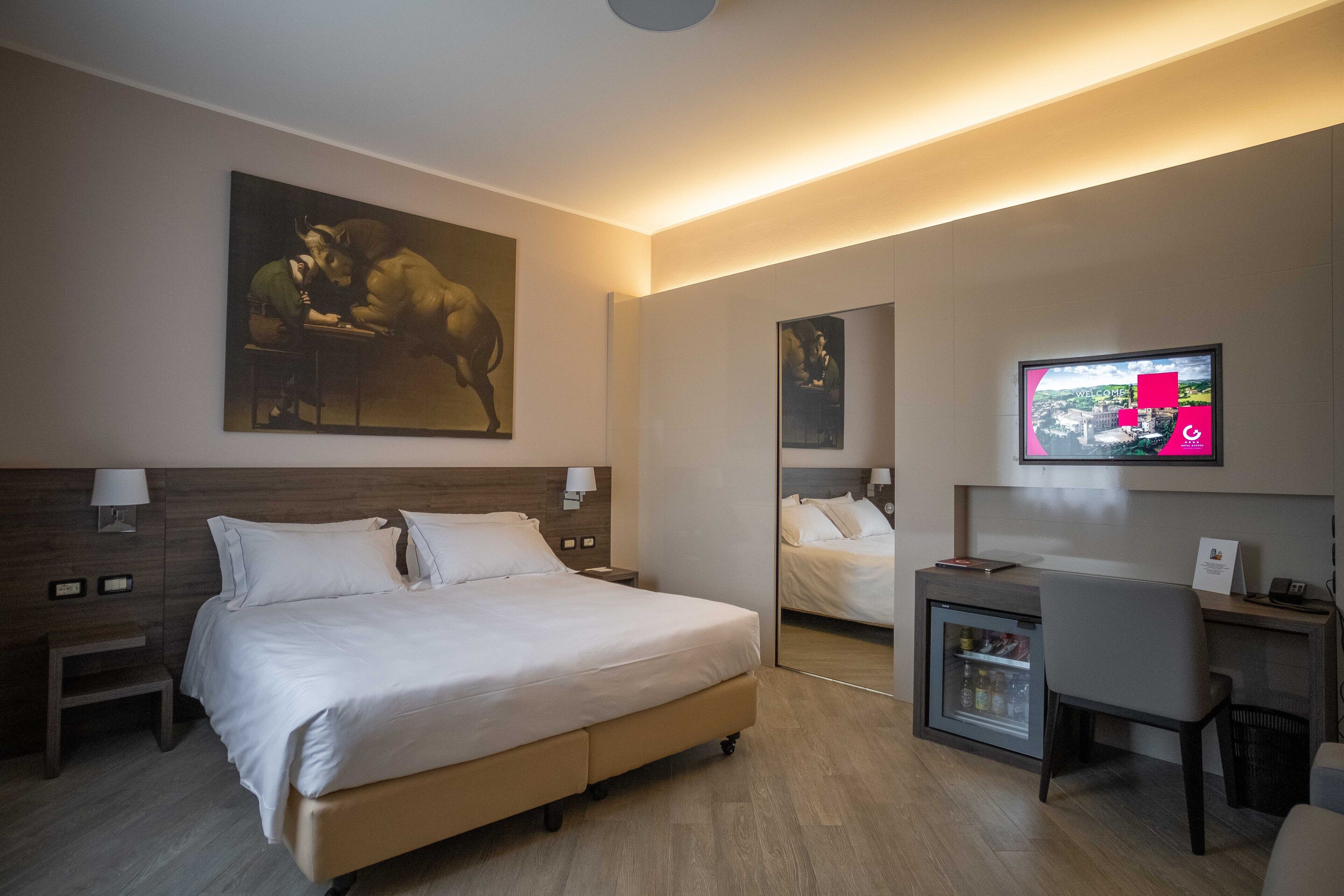 Une chambre d’hôtel moderne avec un grand lit, un bureau, une télévision et un tableau au mur.