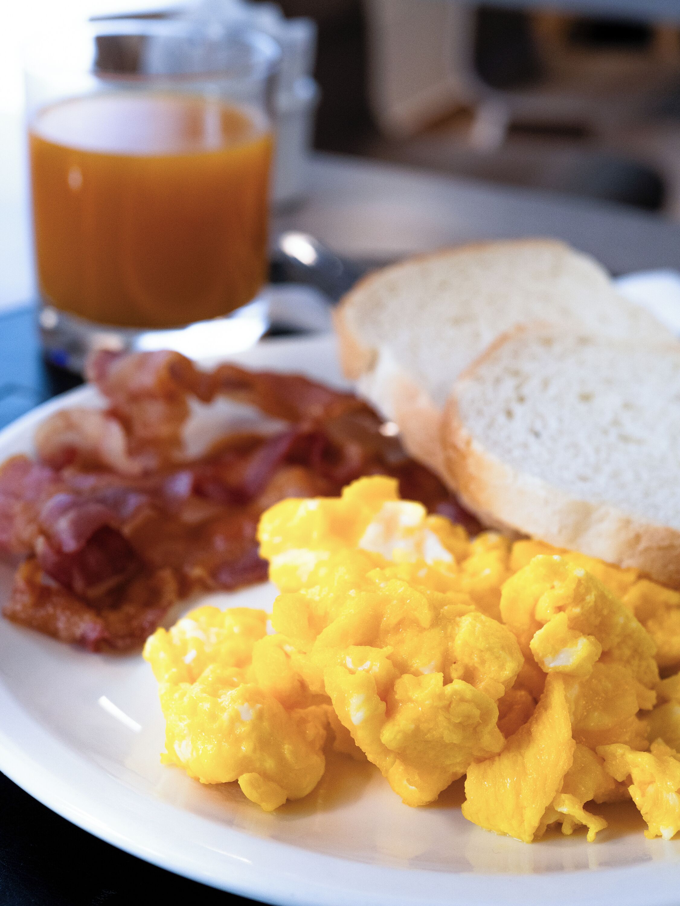 Un plato de huevos revueltos, tocino, tostadas y un vaso de jugo de naranja.