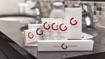 Una encimera de baño con artículos de aseo de Hotel Guerra, incluyendo loción corporal, champú y gel de ducha.