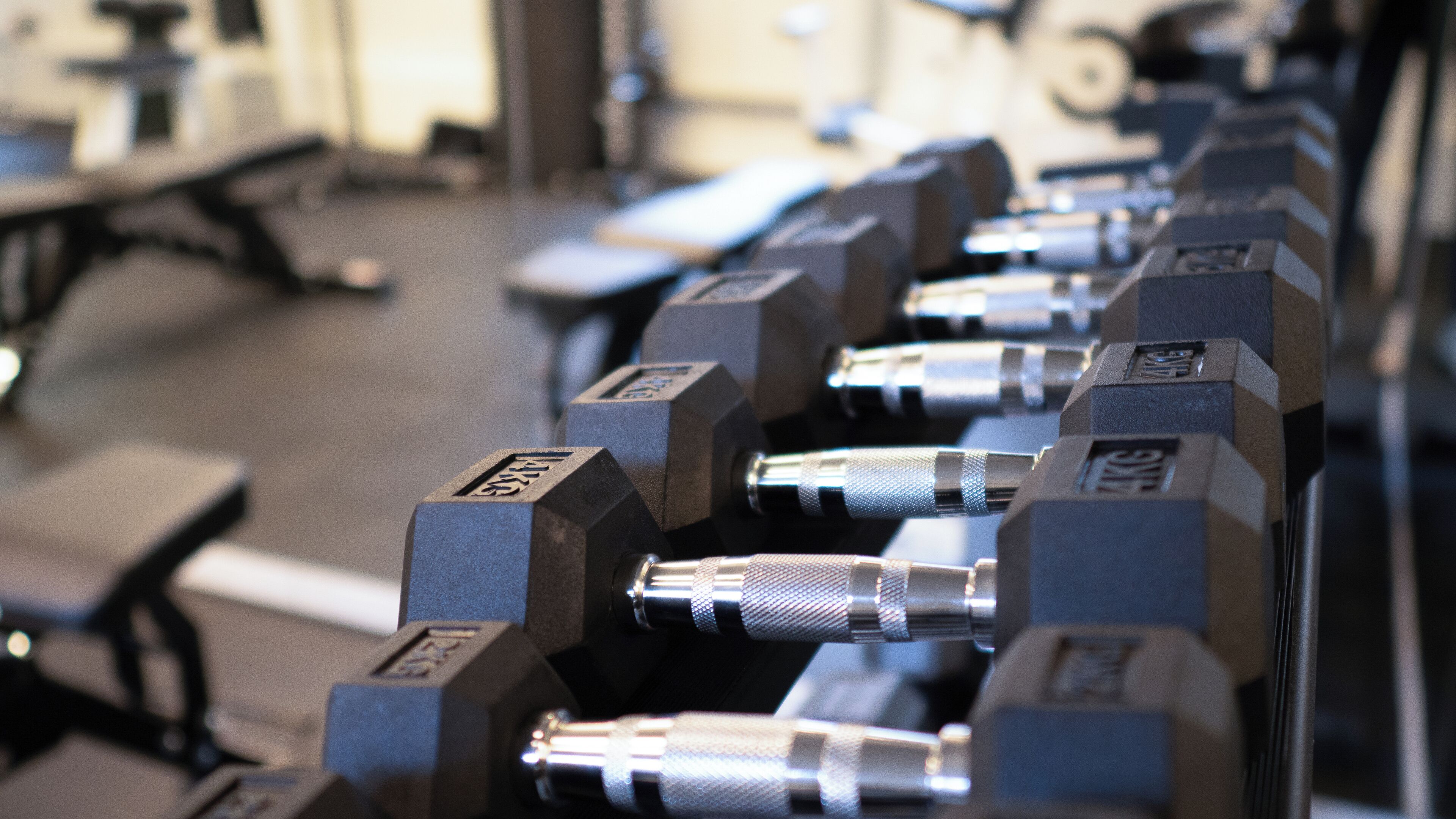 A row of dumbbells with weight markings, arranged on a rack in a gym setting.