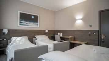A hotel room with two beds, a desk, a chair, a nightstand, and a wall-mounted lamp.