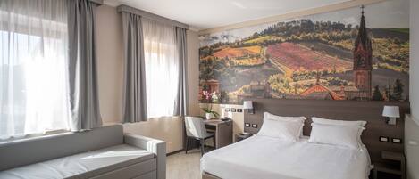 A hotel room with a bed, a sofa, a desk, and a large mural of a landscape.