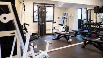 Ein Fitnessstudio mit verschiedenen Trainingsgeräten, darunter Kraftgeräte, Bänke und Kurzhanteln.