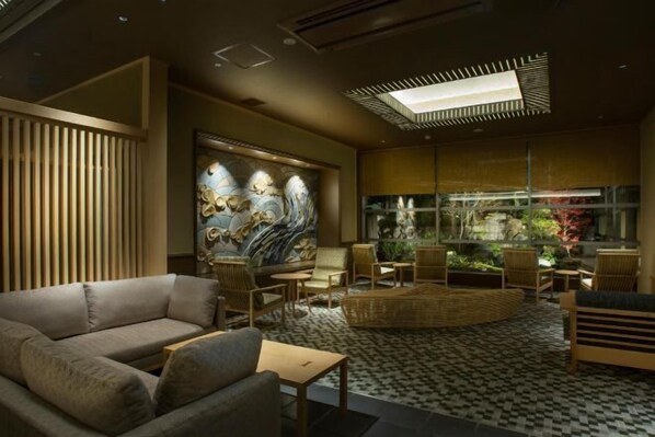 A modern lounge with a sofa, chairs, a patterned floor, a large wall art piece, and a glass enclosure with plants. - Saka Hotel Kyoto (Kyoto)