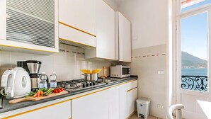 Een moderne keuken met witte kastjes, een gasfornuis, een magnetron en uitzicht op zee door een openslaande balkondeur.