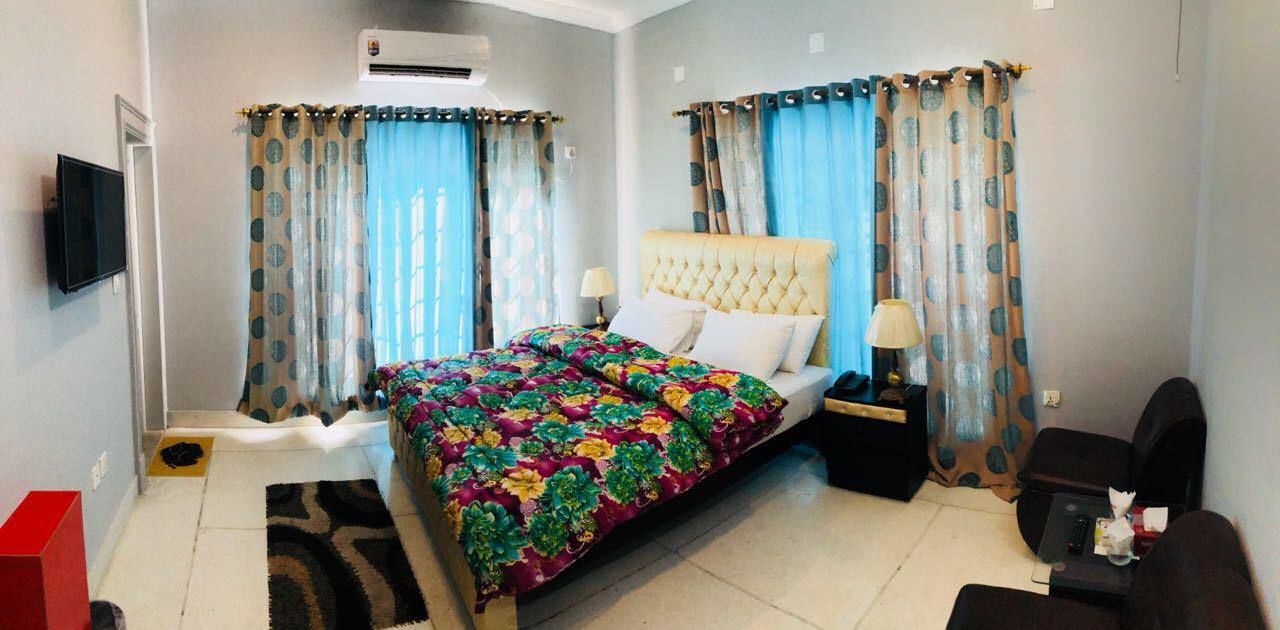 A hotel room with a bed, two bedside tables, a TV, and curtains.